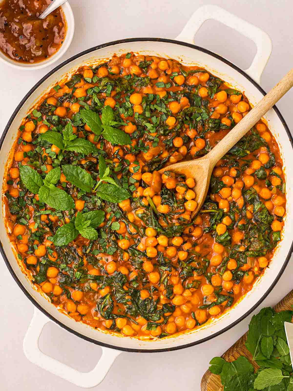 A pan filled with Chickpea Curry, ready to serve with a wooden spoon.