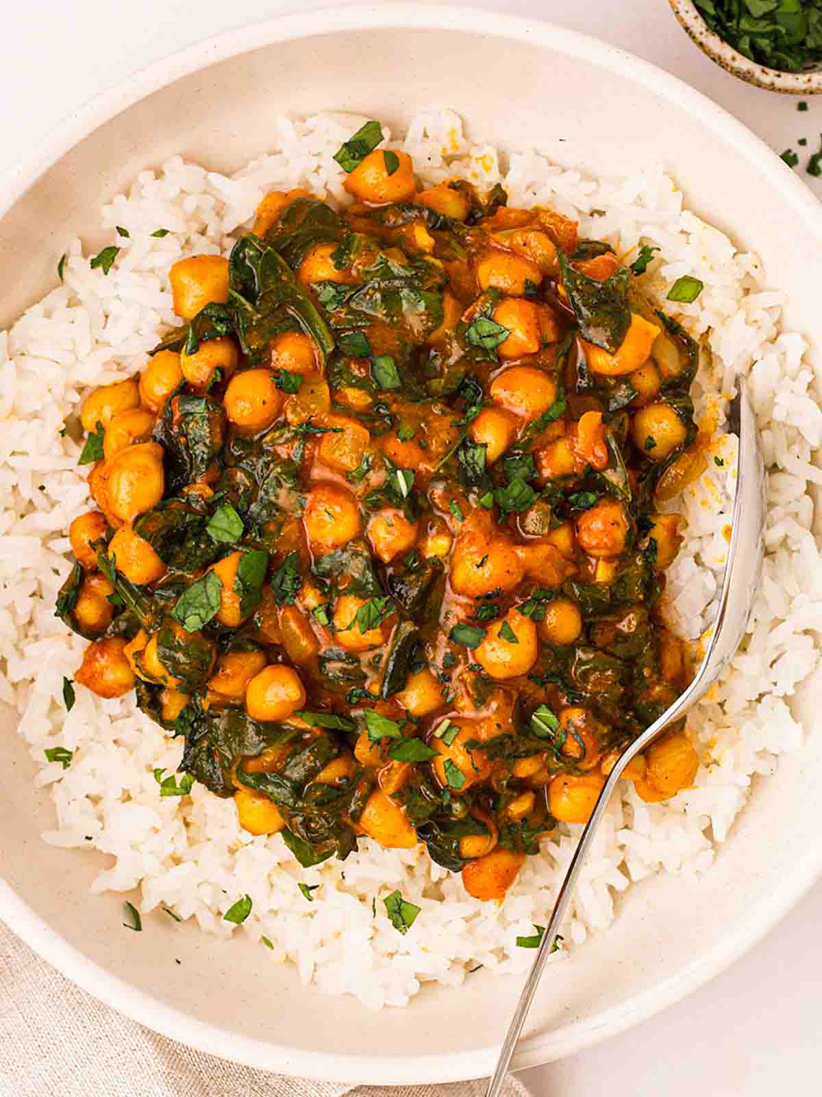 A plate filled with white rice and chickpea curry on top, with a silver spoon to eat.