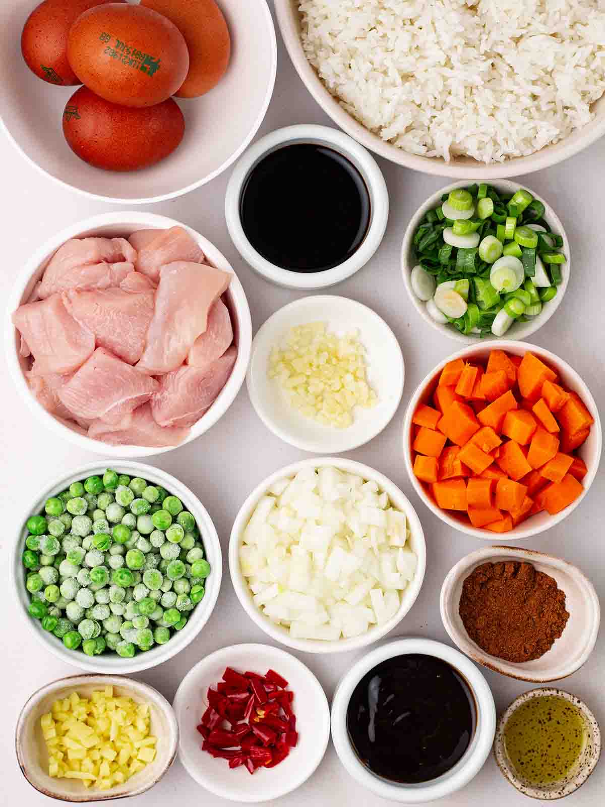 The raw ingredients for making Chicken Fried Rice laid out in small bowls on a white counter top.