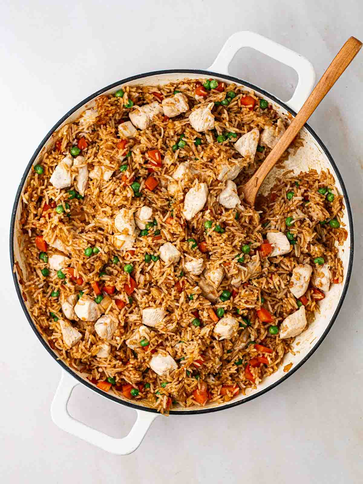 A big pan of chicken fried rice being stirred with a wooden spoon.