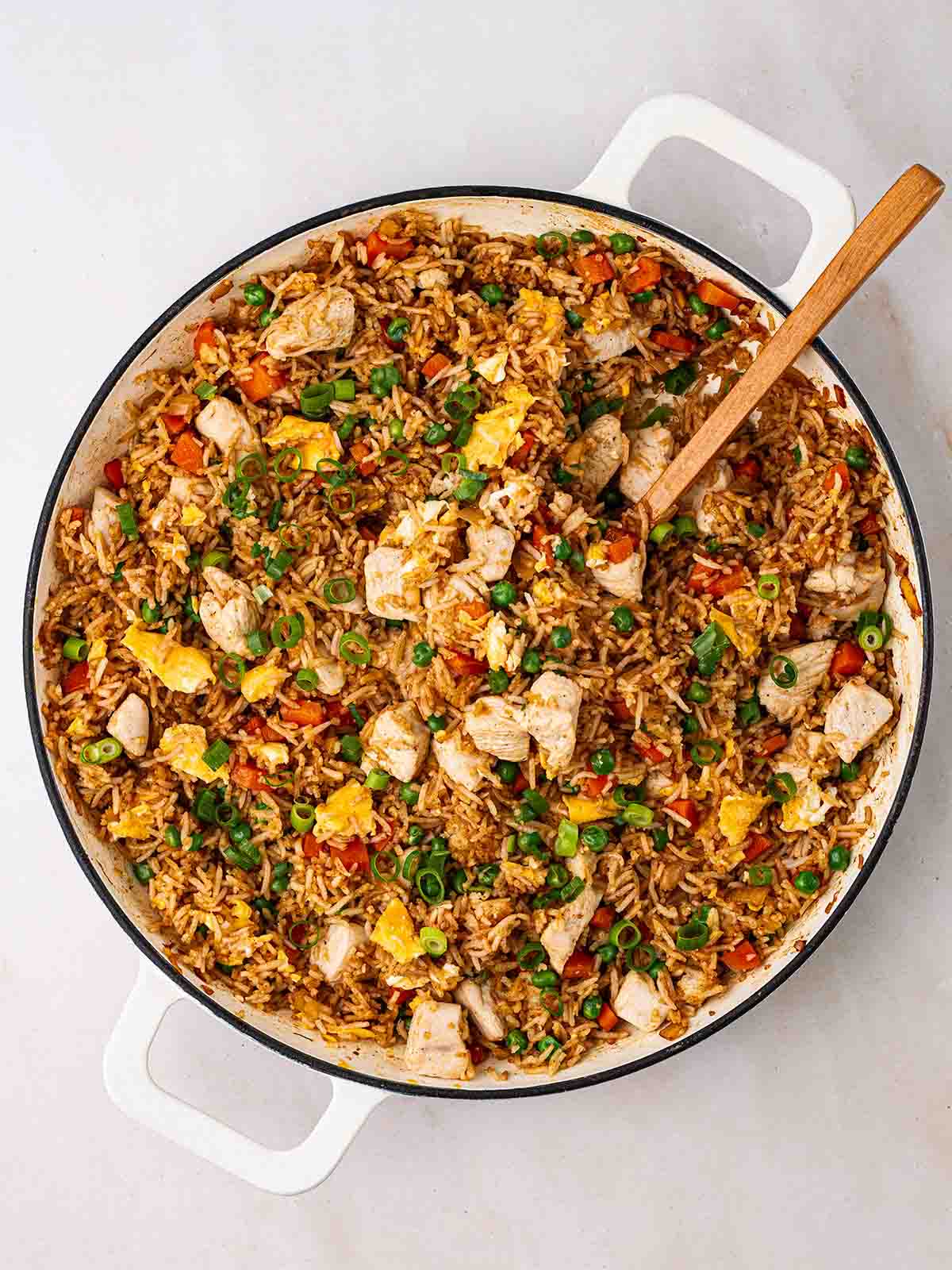 A big pan of Chicken Fried Rice with a wooden spoon stirring.