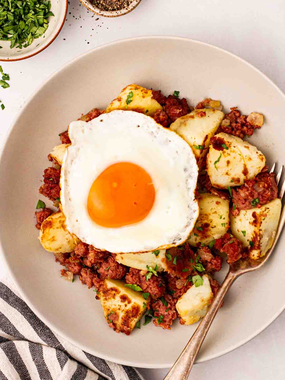 A plate of Corned Beef Hash with a fried egg on top, and a fork stuck in, ready to eat.