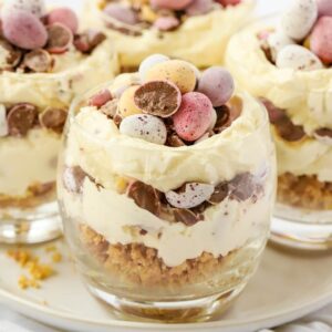 A close up of a tumbler filled with layers of Mini Cheesecakes for Easter, with a biscuit base, layers of cream and Cadbury's Mini Eggs.