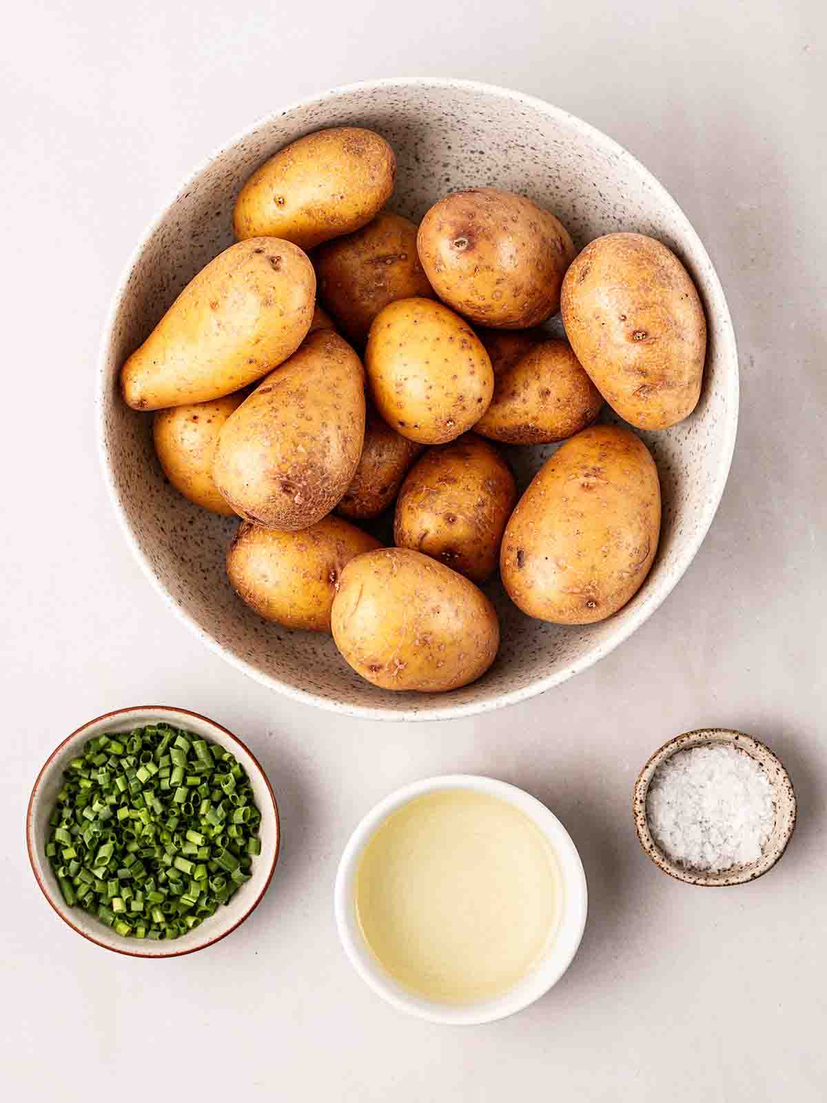 The ingredients for making Sautéed Potatoes laid out in bowls on a white surface.