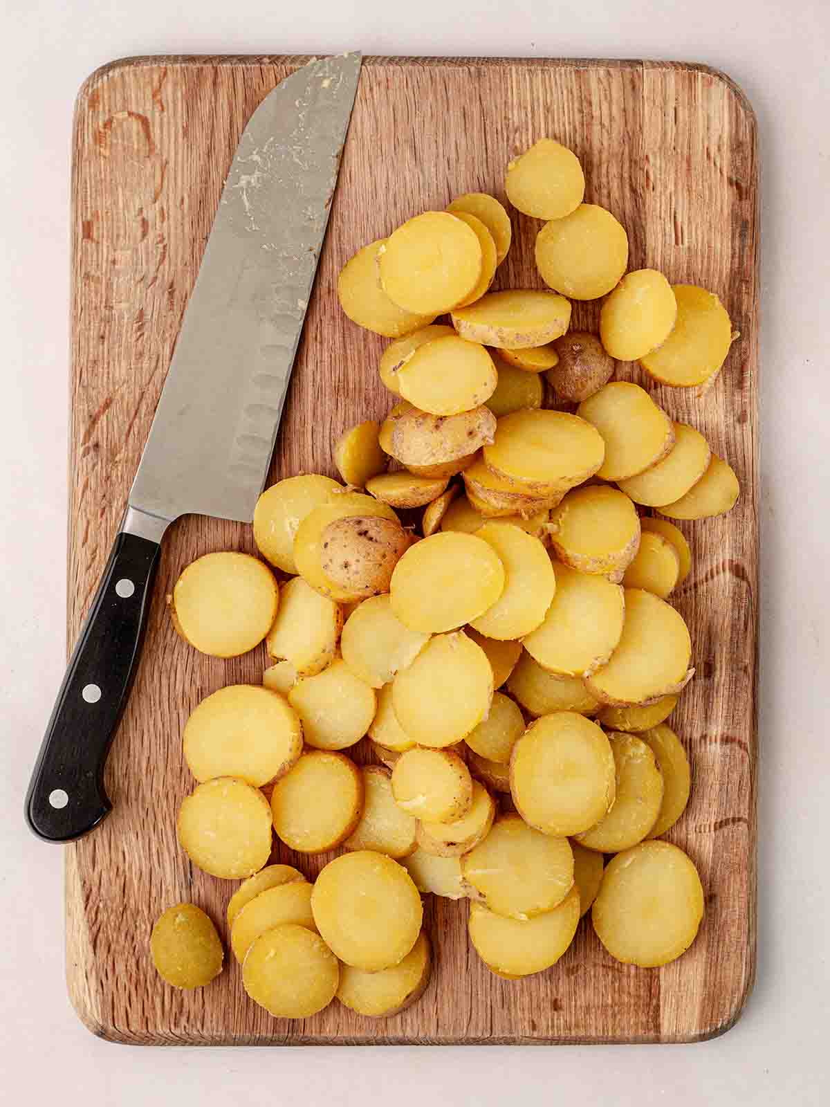 A chopped board with sliced white potatoes and knife to the side, for step 1 in the recipe for Sautéed Potatoes.