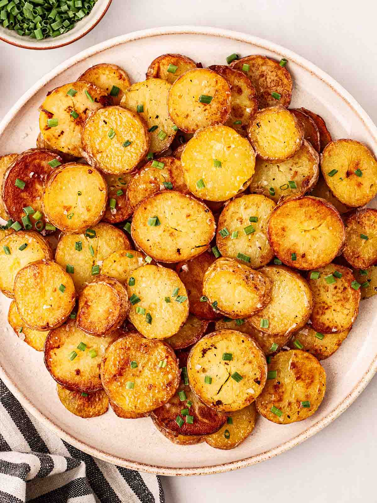 A white plate filled with lots of golden, crunchy sautéed potatoes, on a table as a side dish.