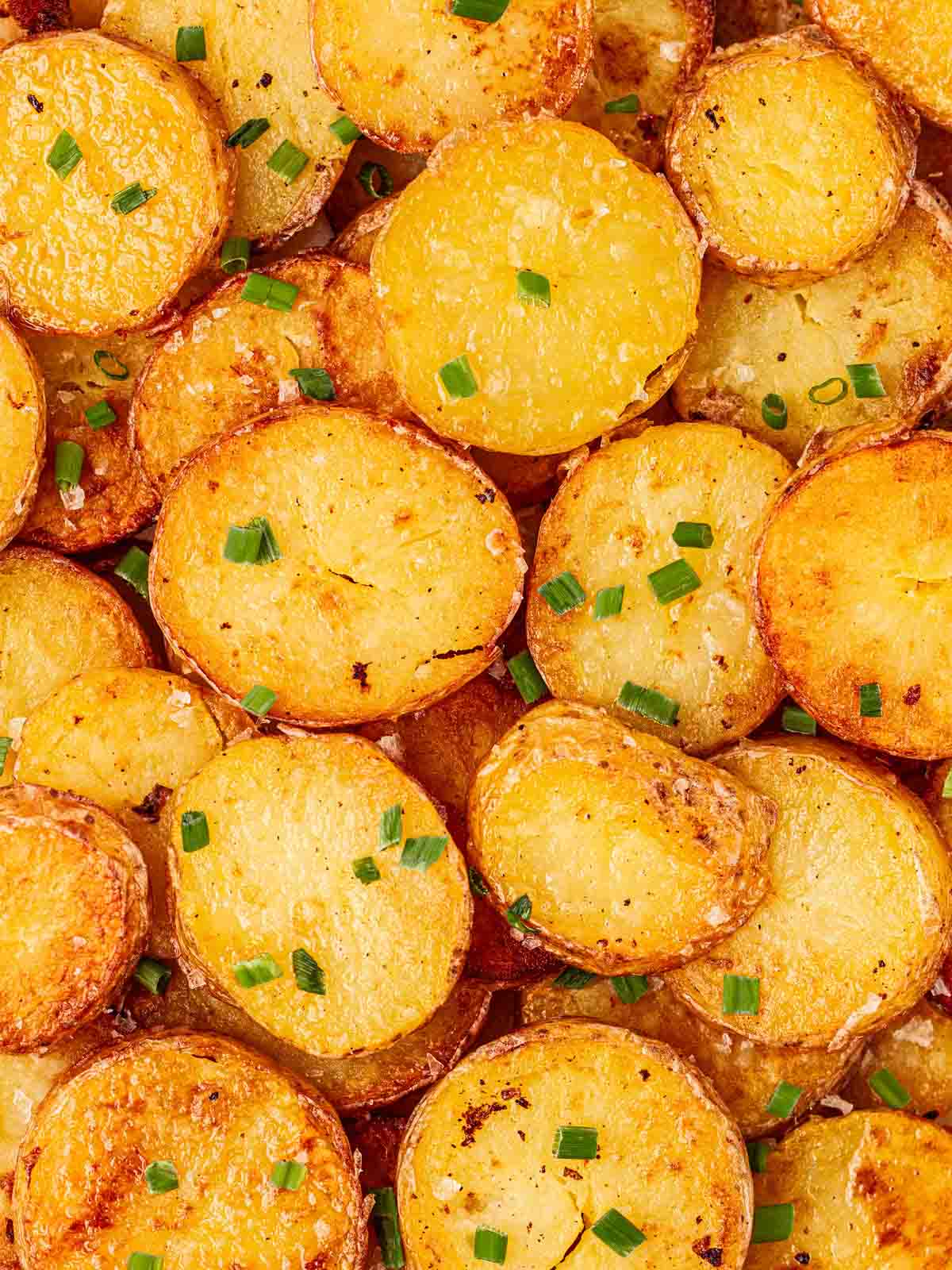A close up of round golden sautéed potatoes, with green chives sprinkled over to garnish.