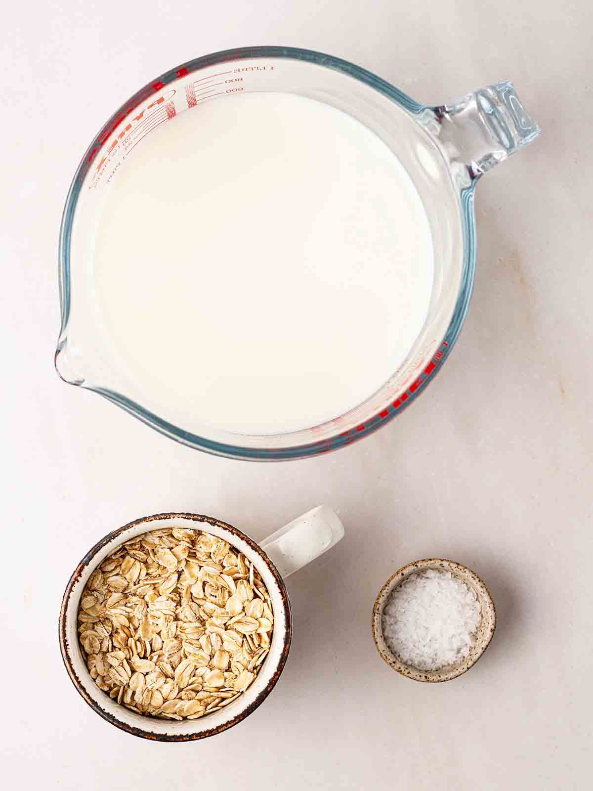 The ingredients for making slow cooker porridge laid out on a white counter: milk, oats and salt.