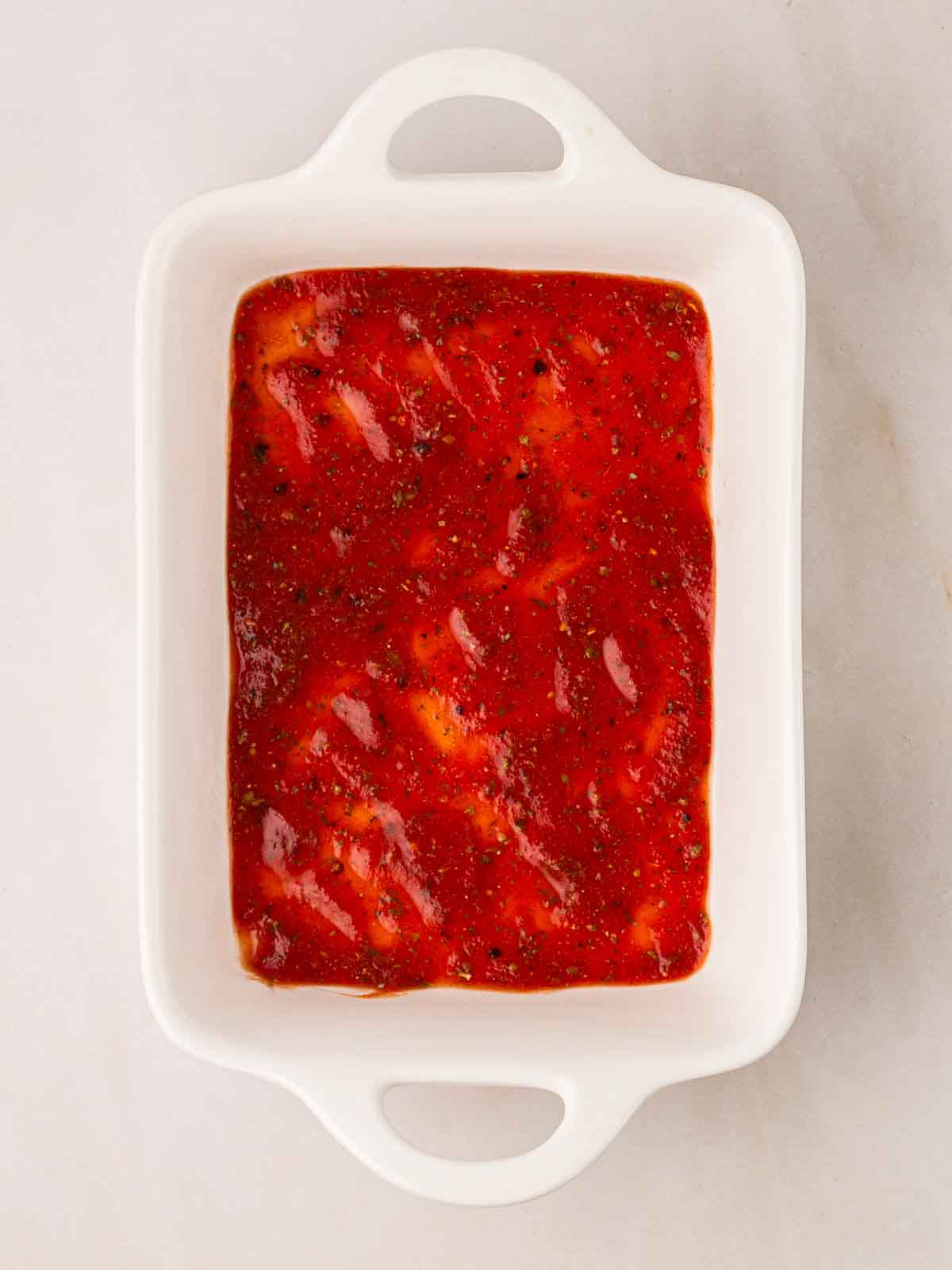 An oven dish with a layer of tomato sauce for step 4 in the recipe for Spinach and Ricotta Cannelloni.