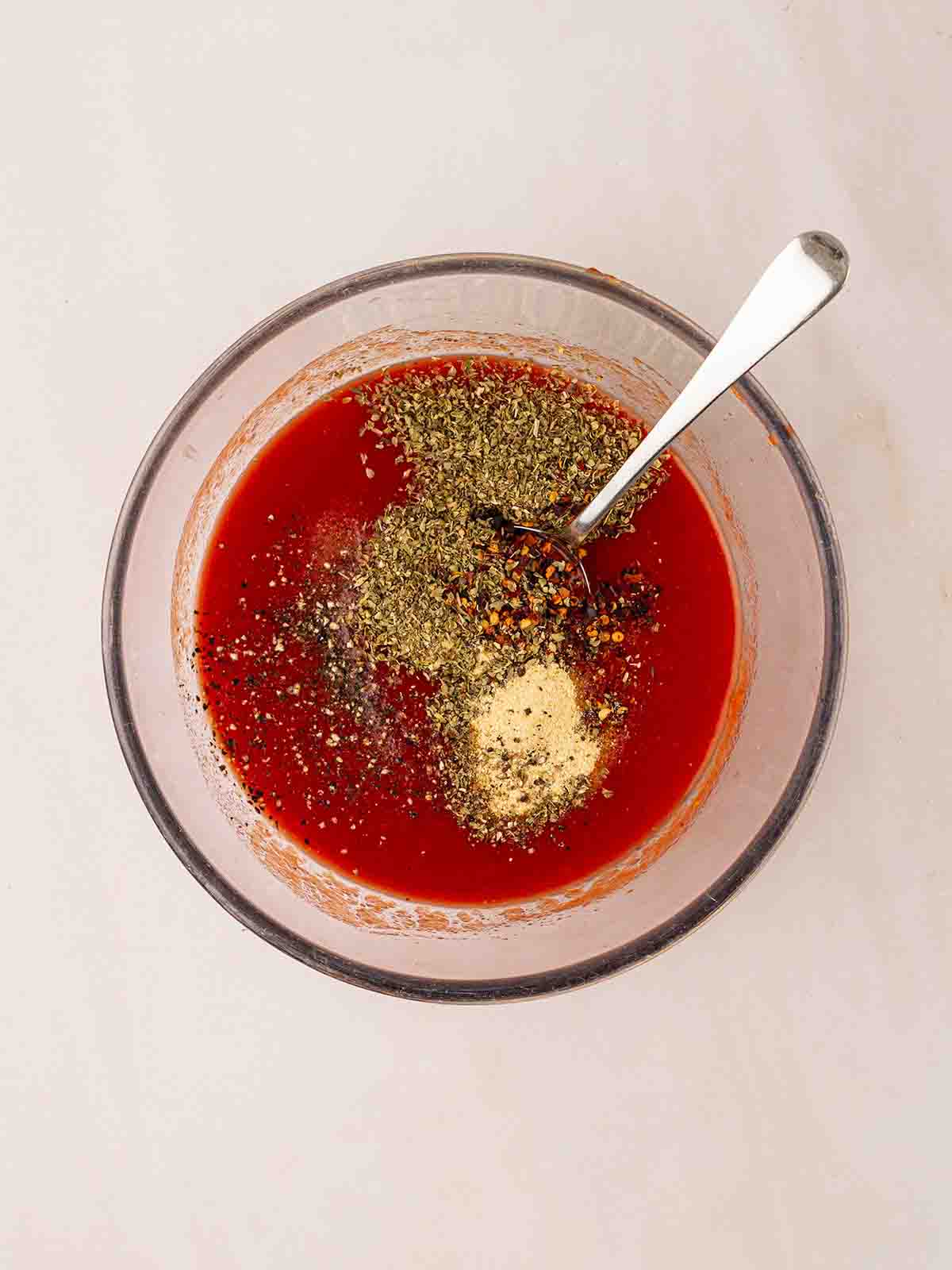 A glass bowl filled with tomato sauce, herbs and spices for step 2 in the recipe for Spinach and Ricotta Cannelloni.