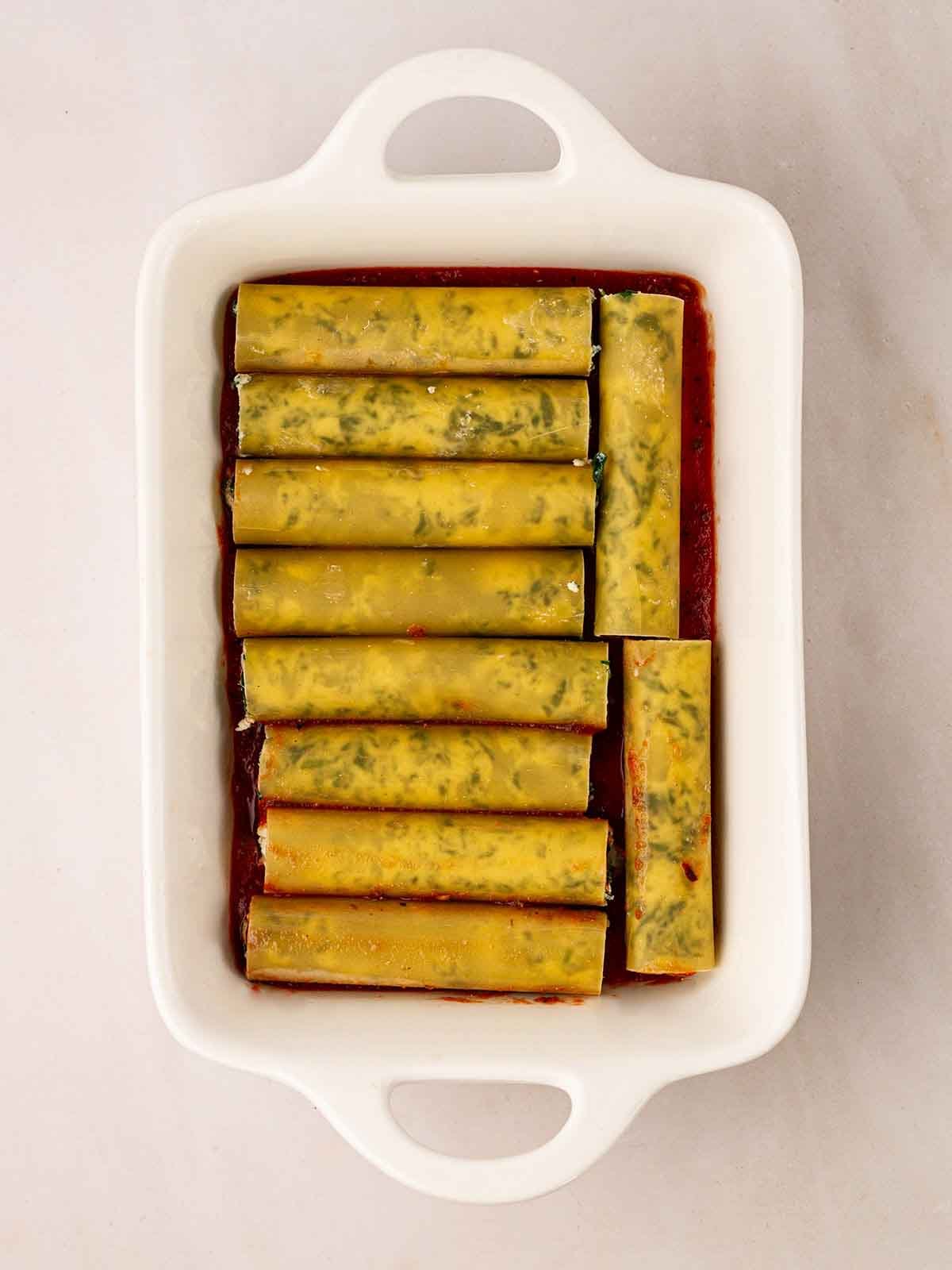 Unbaked cannelloni tubes filled with spinach and ricotta on a bed of tomato sauce for step 6 in the recipe for Spinach and Ricotta Cannelloni.