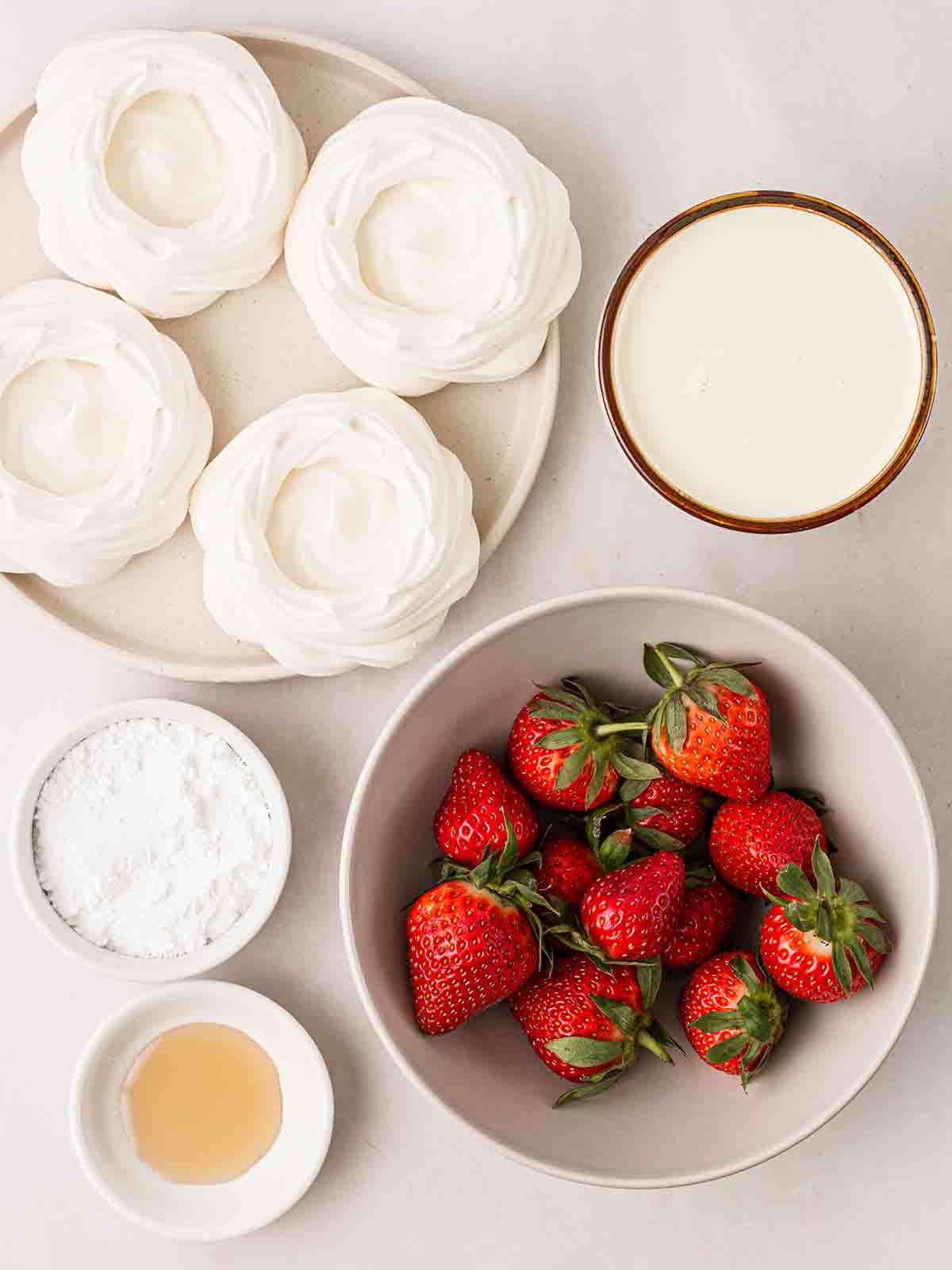 The ingredients for making Eton Mess laid out individually in bowls on a white surface.