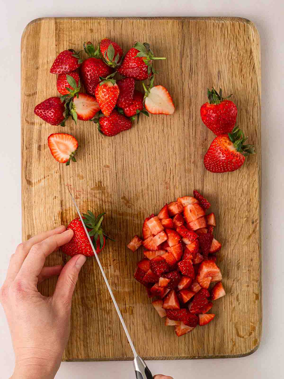 A chopping board filled with strawberries being chopped up for Eton Mess.