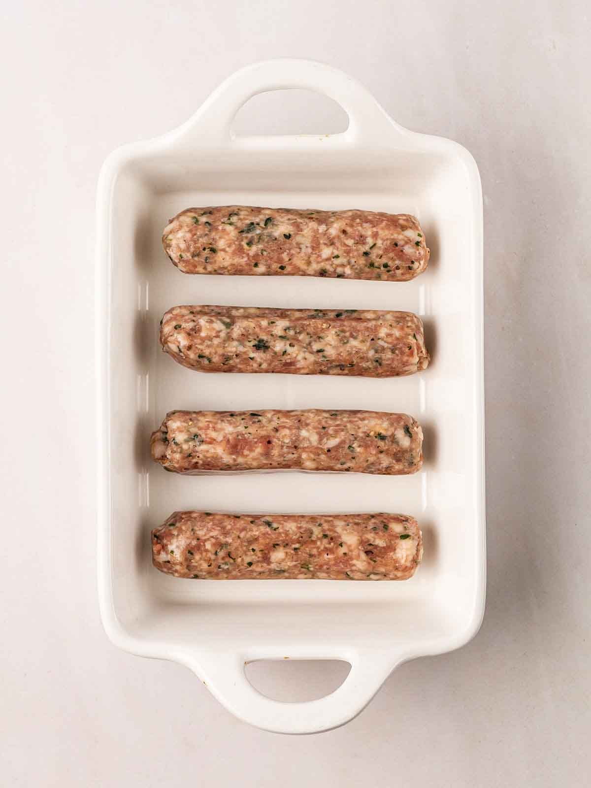 A white oven dish filled with raw sausages for step 1 in the recipe for a Full English Breakfast.