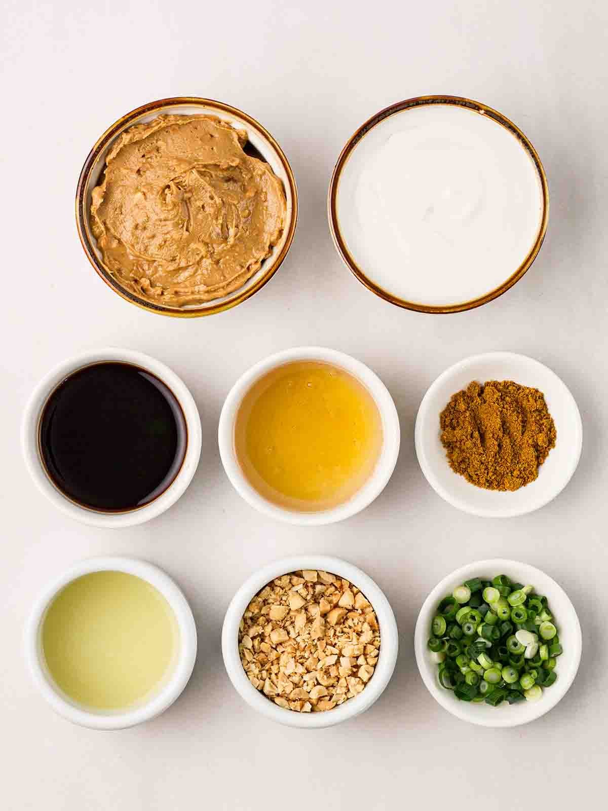 The ingredients for making homemade Satay Sauce laid out in small bowls on a white counter.