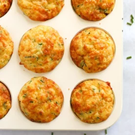 Cheese and sweetcorn savoury muffins in a muffin tin, just baked and golden on top.