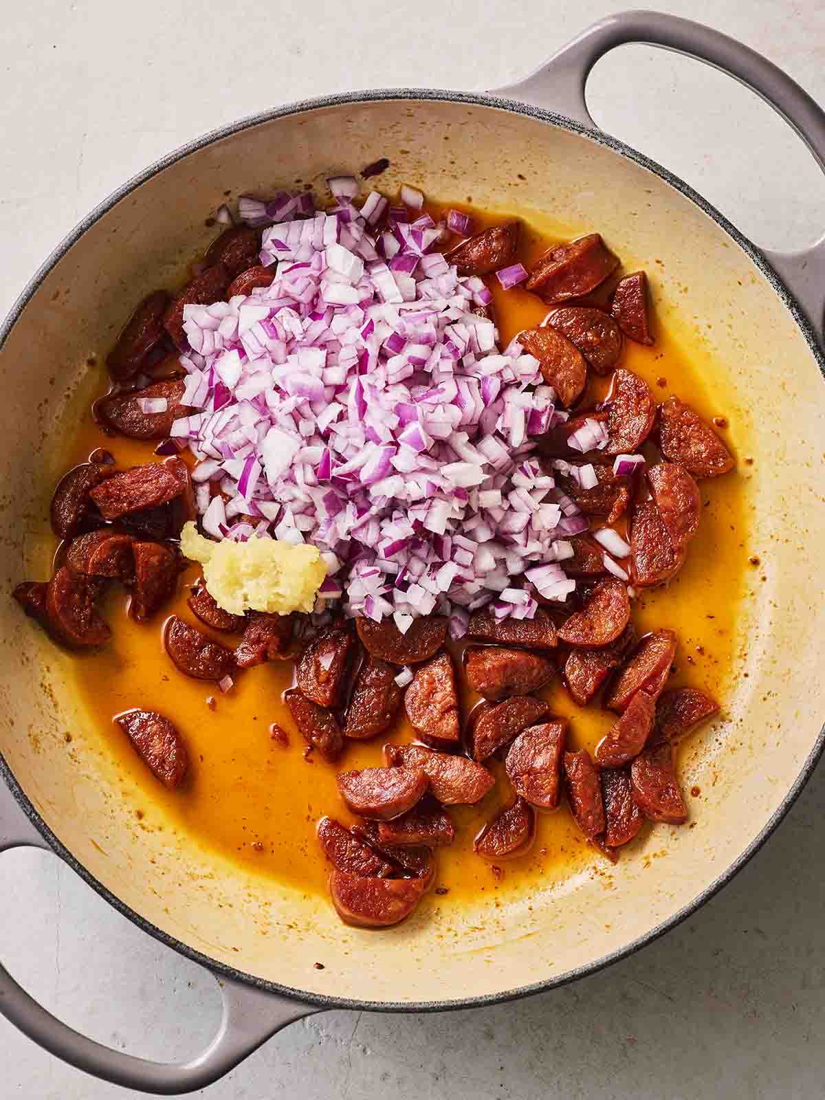 A pan filled with chorizo, onion and garlic for step 2 in the recipe for Chorizo Orzo pasta.