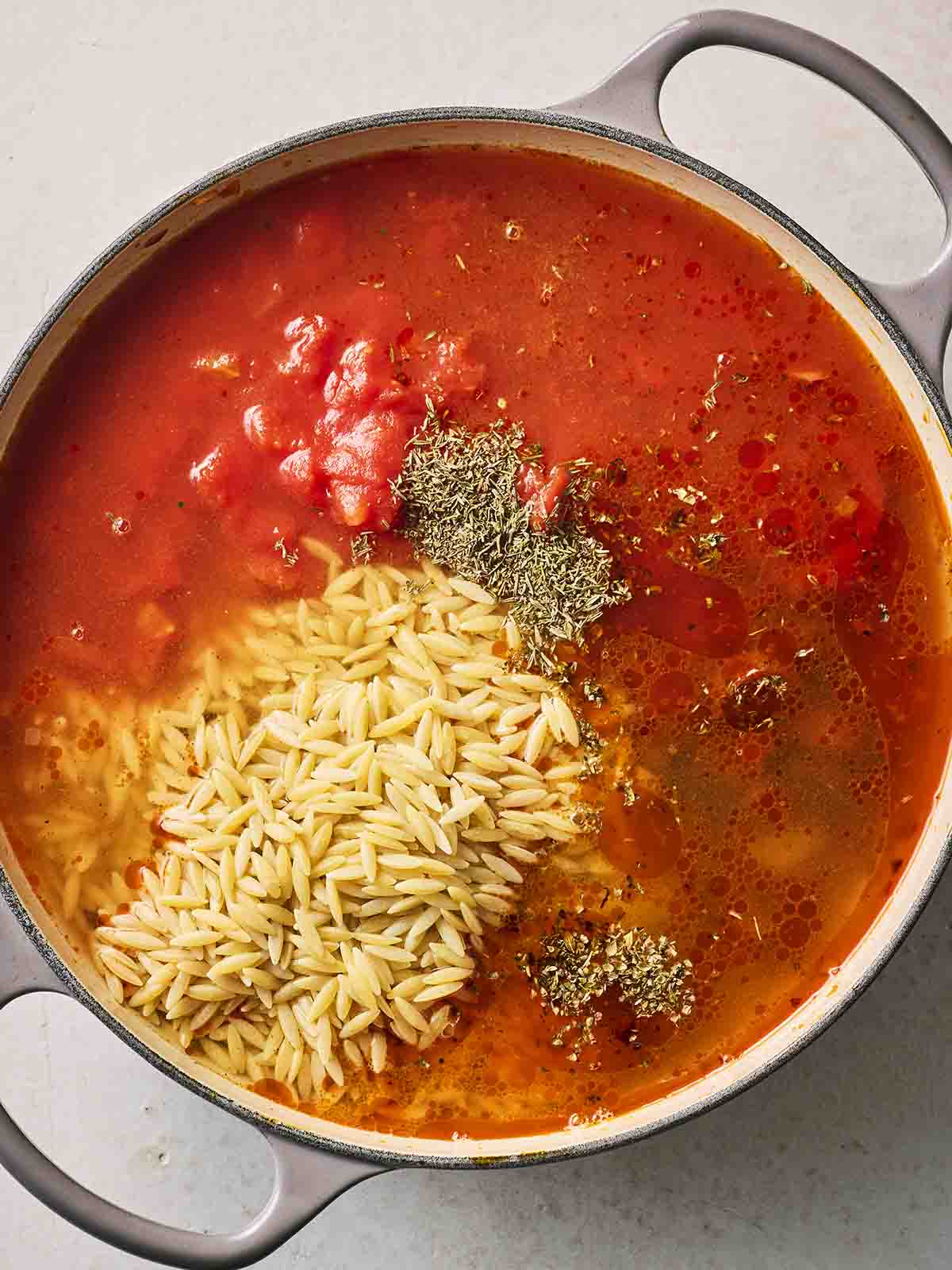 A pan filled with tomato sauce, uncooked orzo, herbs and spices and chorizo for step 3 in the recipe for how to make easy Chorizo Orzo.