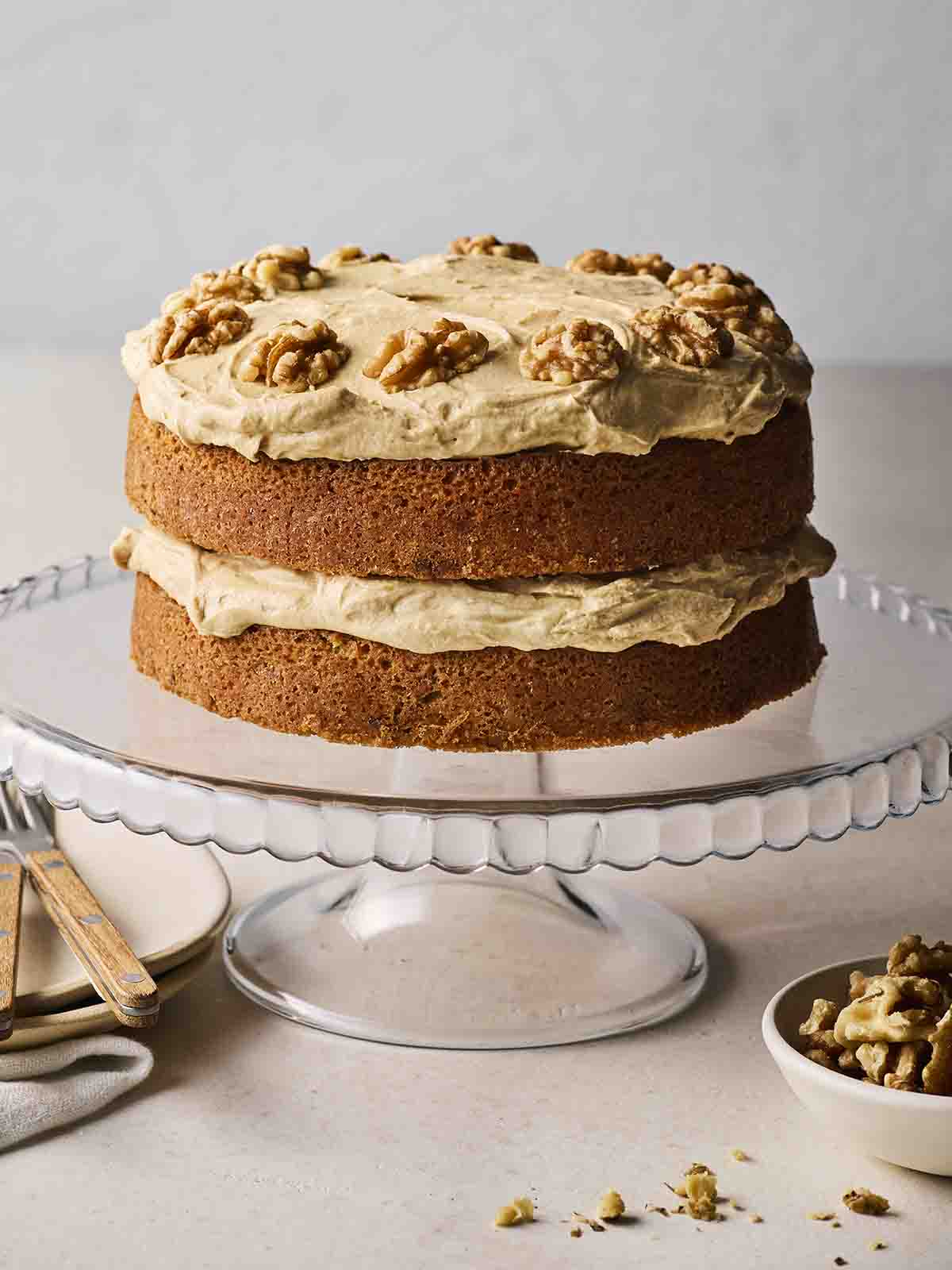 A glass cake stand with a freshly baked Coffee and Walnut Cake on top.