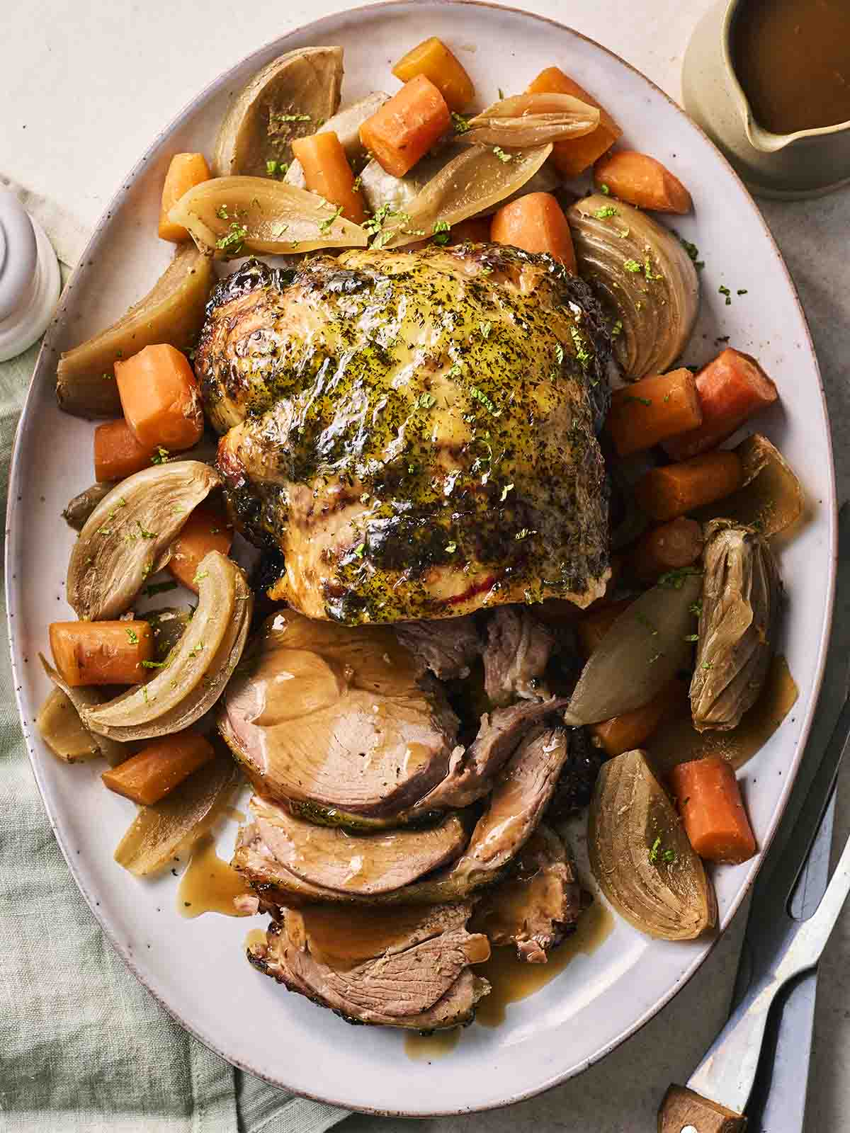 A serving plate with a leg of lamb in the middle, surrounded by cooked vegetables, straight out of the slow cooker.