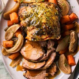 A slow cooker leg of lamb on a plate, ready to serve, with vegetables around the side.