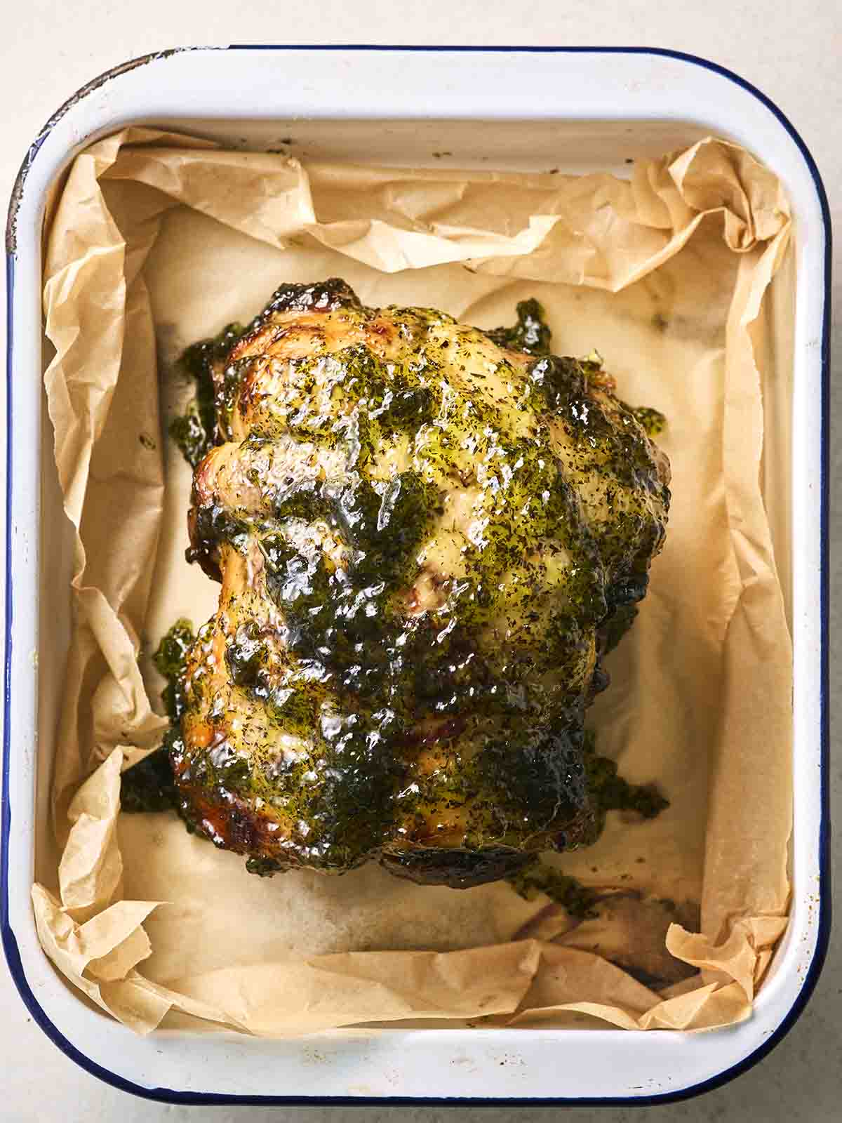 A cooked leg of lamb on an oven tray with mint jelly over the top.