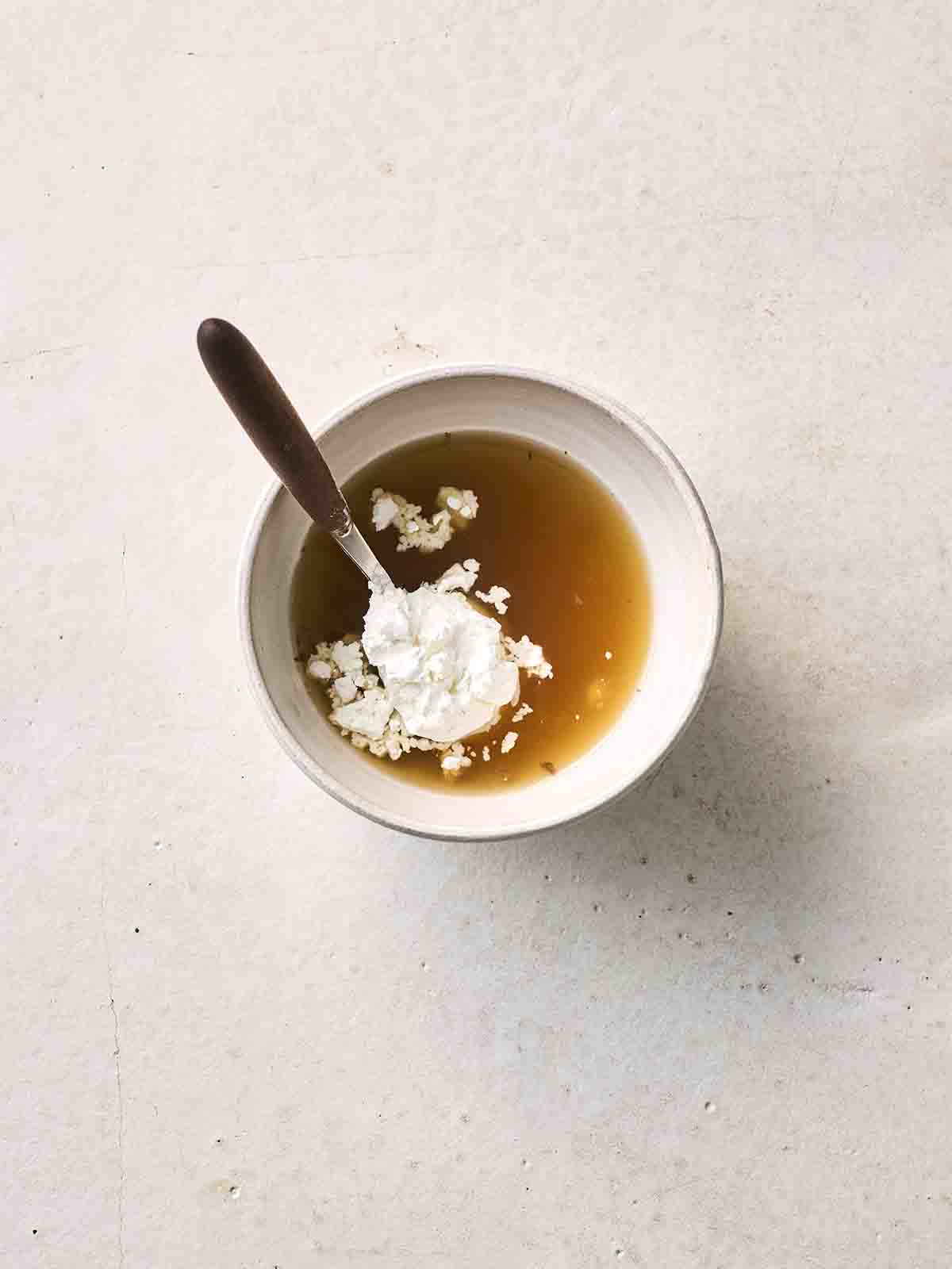 A small white bowl filled with lamb gravy and cornflour with a spoon, ready to thicken into a slurry.