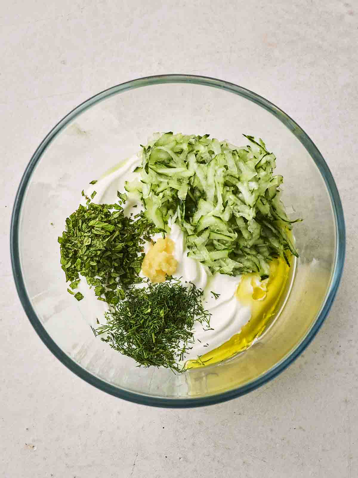 The ingredients for learning how to make Tzatziki in a glass bowl, before being mixed.