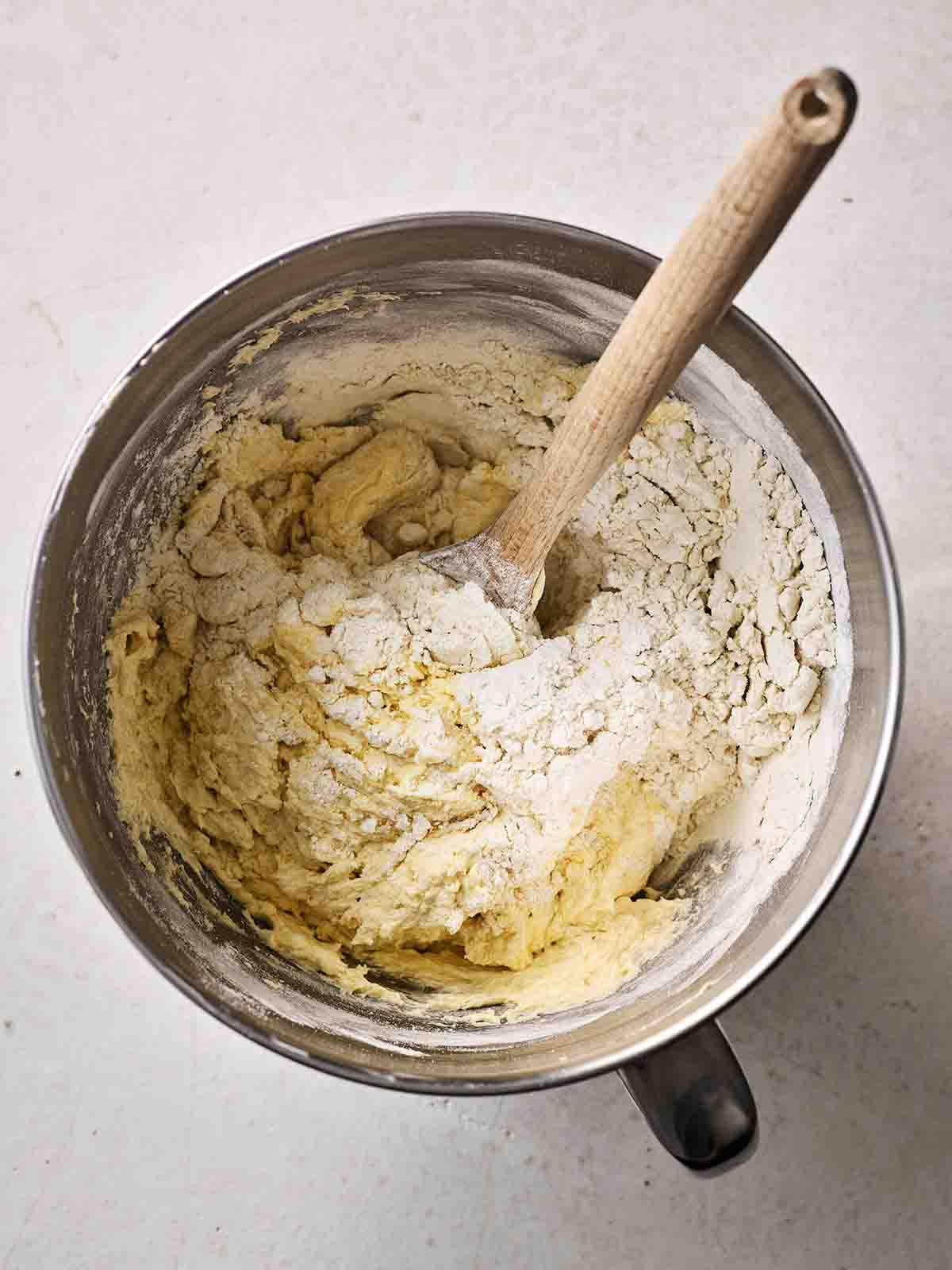 A mixing bowl with flour being stirred into the batter with a wooden spoon, for step 3 in the recipe for Victoria Sponge.