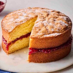 A Victoria Sponge Cake with a piece missing on a plate, ready to eat.