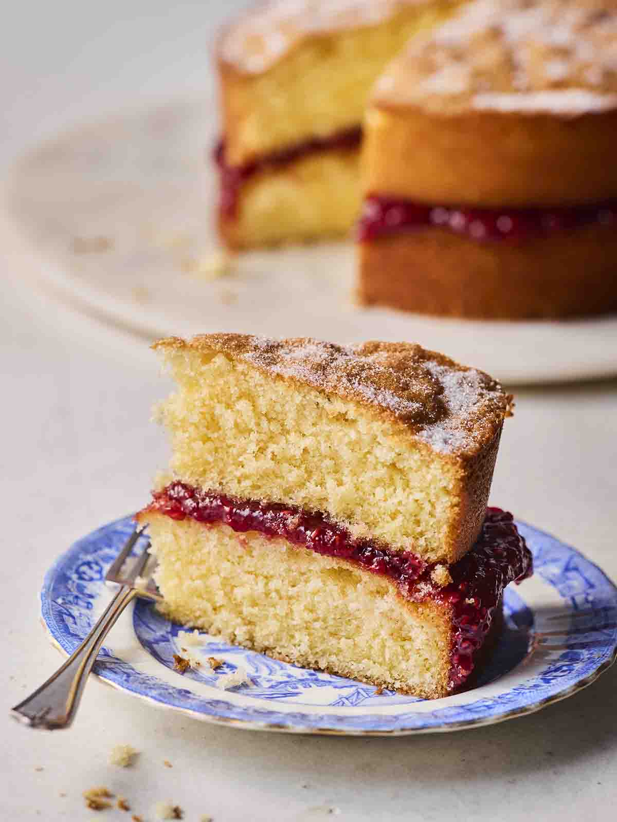 A slice of Victoria Sponge on a blue cake plate with a fork, ready to eat.