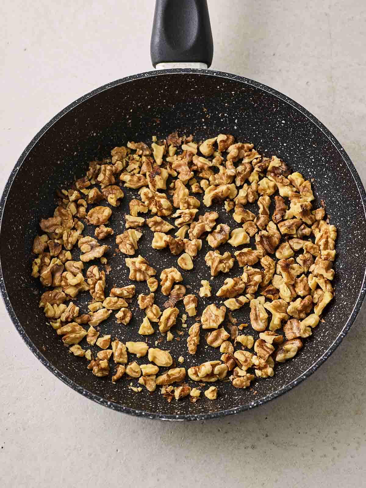 A black frying pan with chopped walnuts frying, for step 1 in the recipe for Waldorf Salad.