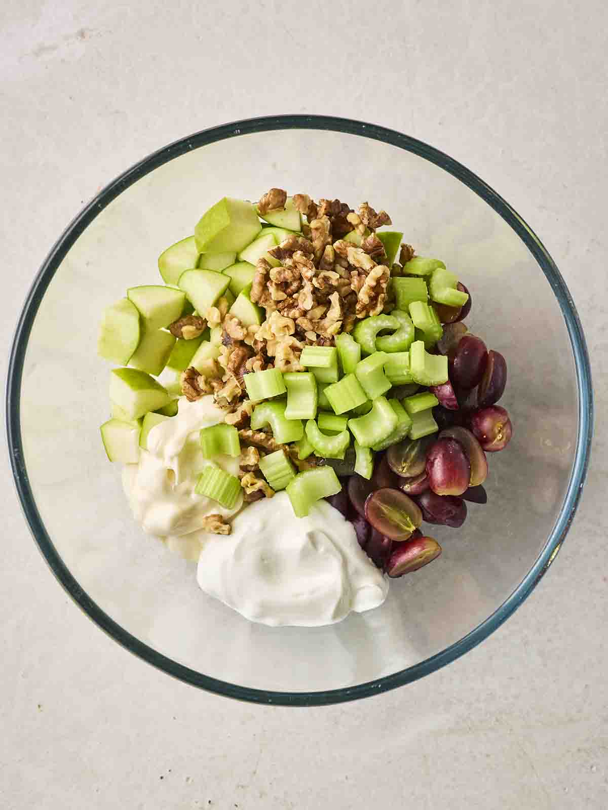 The chopped ingredients for a Waldorf Salad in a glass bowl, ready to be mixed, for step 2 in the recipe.