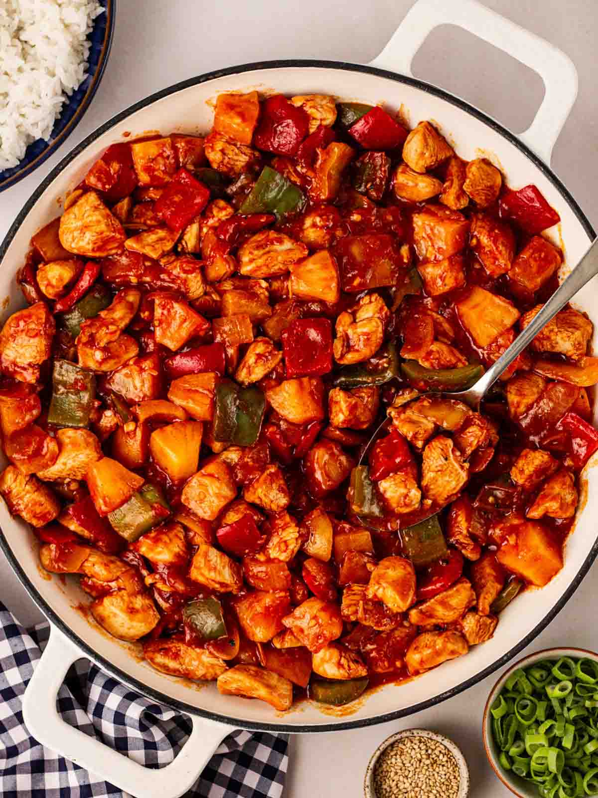 A white pan on a dining table filled with cooked Sweet and Sour Chicken, ready to serve.
