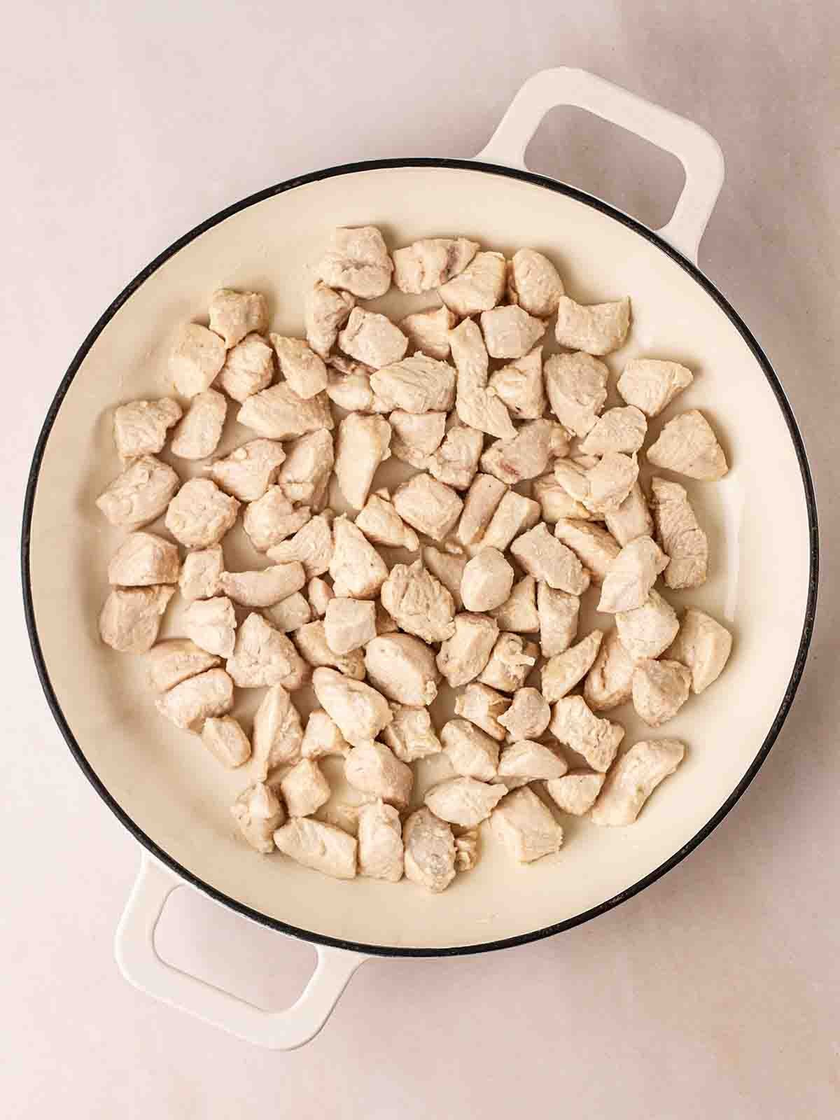 A white pan filled with cooked pieces of cubed chicken breast, for step 1 in the recipe for Sweet and Sour Chicken.