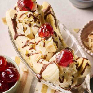 A classic Banana Split in a boat dish with cherries on top and melted chocolate.