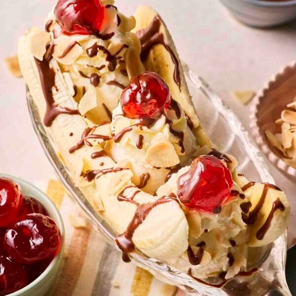 A classic Banana Split in a boat dish with cherries on top and melted chocolate.