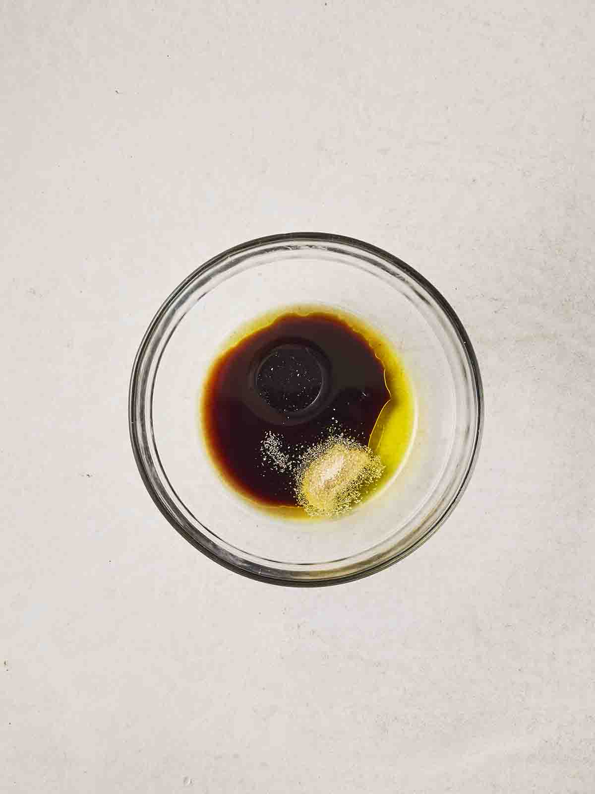 A glass bowl of olive oil, balsamic vinegar, garlic granules, salt and pepper.