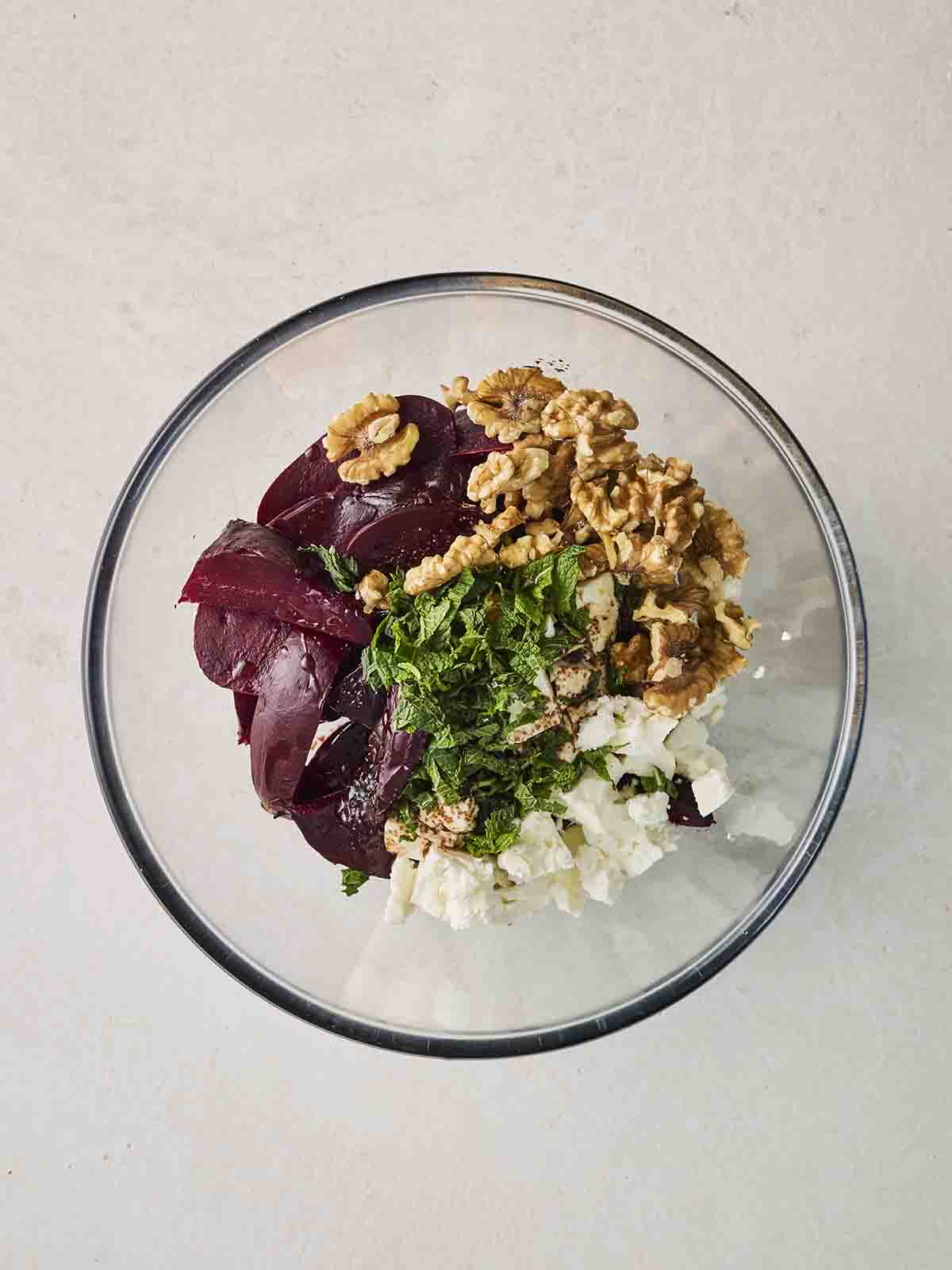 Lots of ingredients that make up a Beetroot Salad in a glass bowl, ready for mixing.