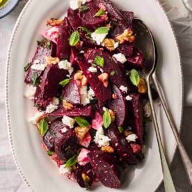 A colourful Beet Salad on a white serving plate with cutlery to serve.