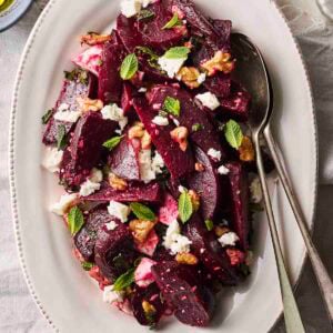 A colourful Beet Salad on a white serving plate with cutlery to serve.