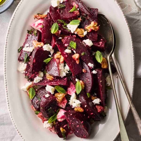 A colourful Beet Salad on a white serving plate with cutlery to serve.