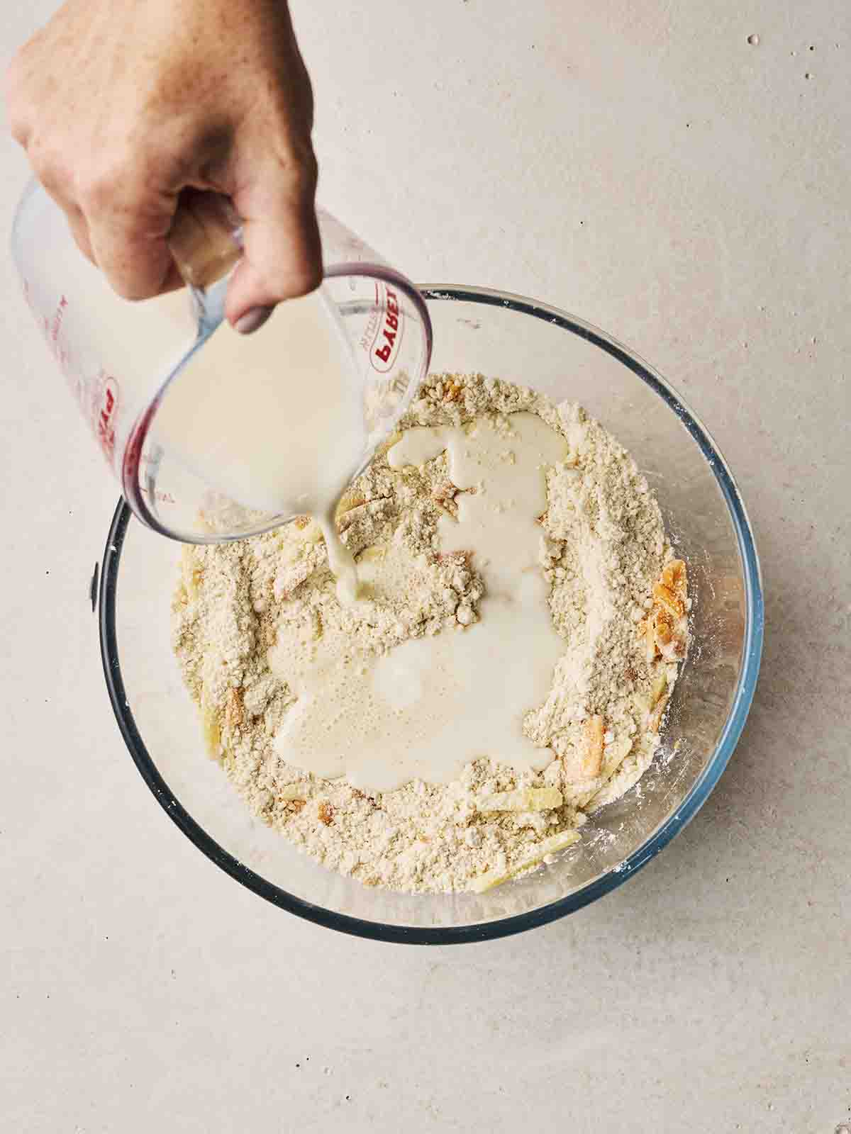 A glass bowl with milk being poured into flour mixture and grated cheese for step 2 in the recipe for Cheese Scones.