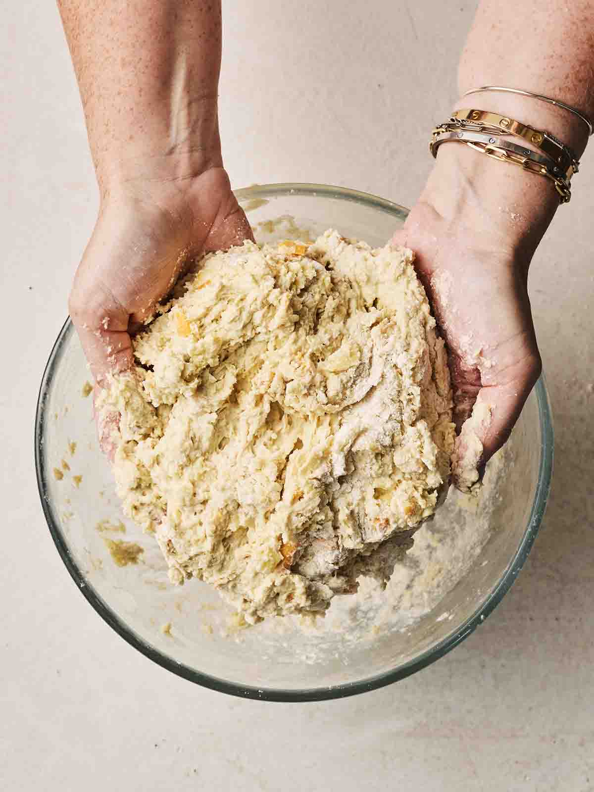 Two hands showing a Cheese Scone dough over a glass bowl.