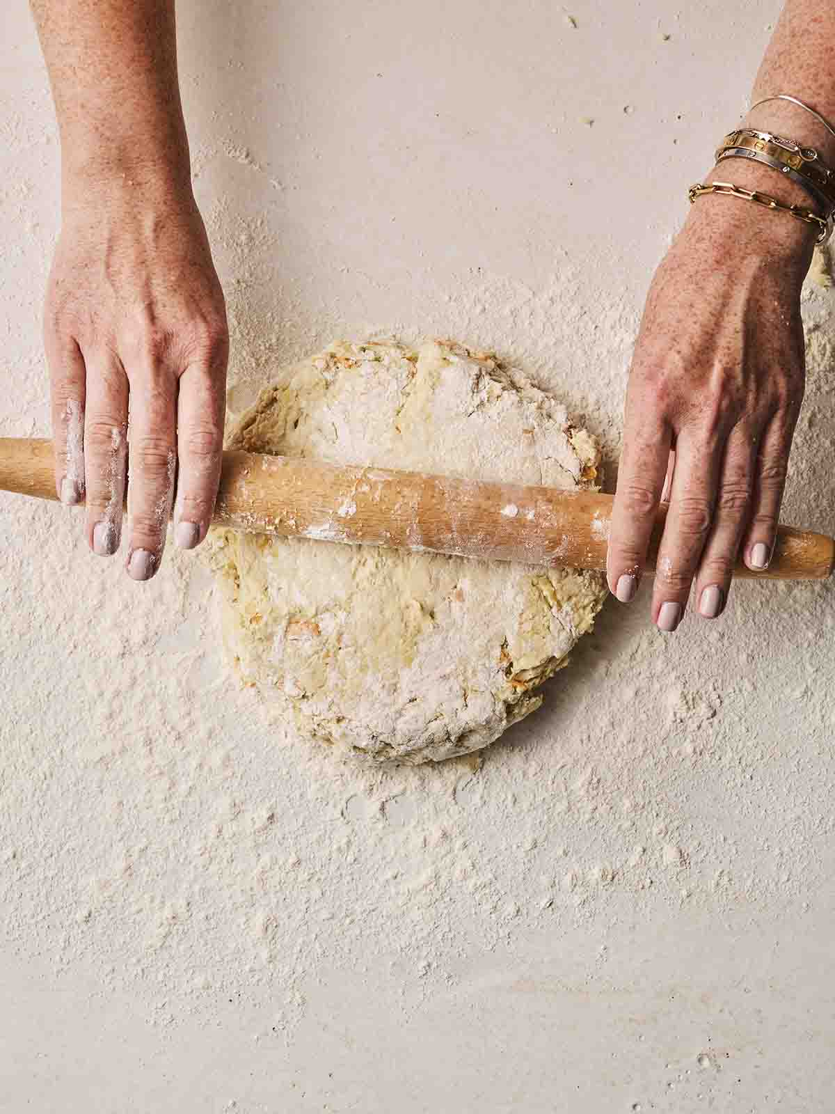 Two hands rolling out a floury mixture with a rolling pin for making Cheese Scones.