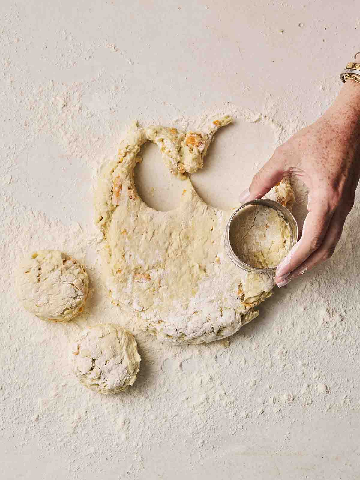 A hand using a cutter on a floury dough for making Cheese Scones.