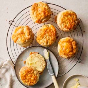 Baked Cheese Scones on a wire rack with a side plate and knife, with one scone buttered.