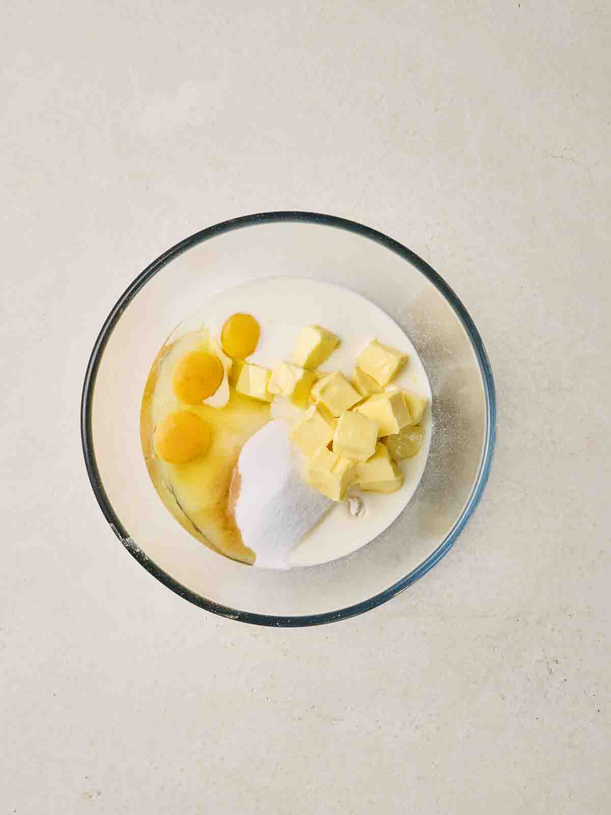Cubes of butter, eggs, sugar and flour in a glass bowl.