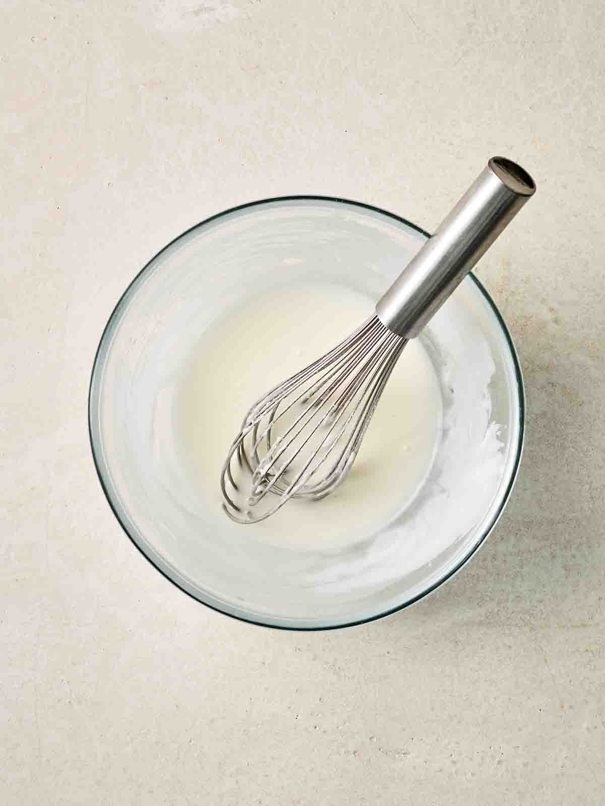 A glass bowl filled with icing and a whisk.