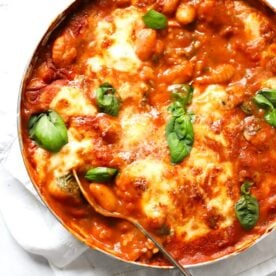 A large pan of cooked Gnocchi Bake with mozzarella and basil on top, with a spoon ready to serve.